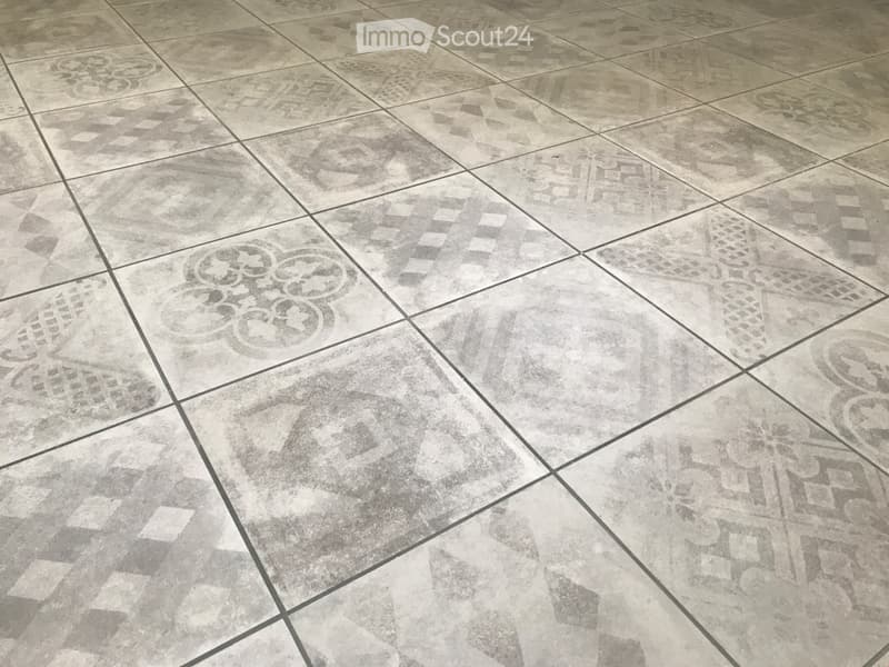Empty room with a decorative tile floor featuring geometric and floral patterns in grey tones.