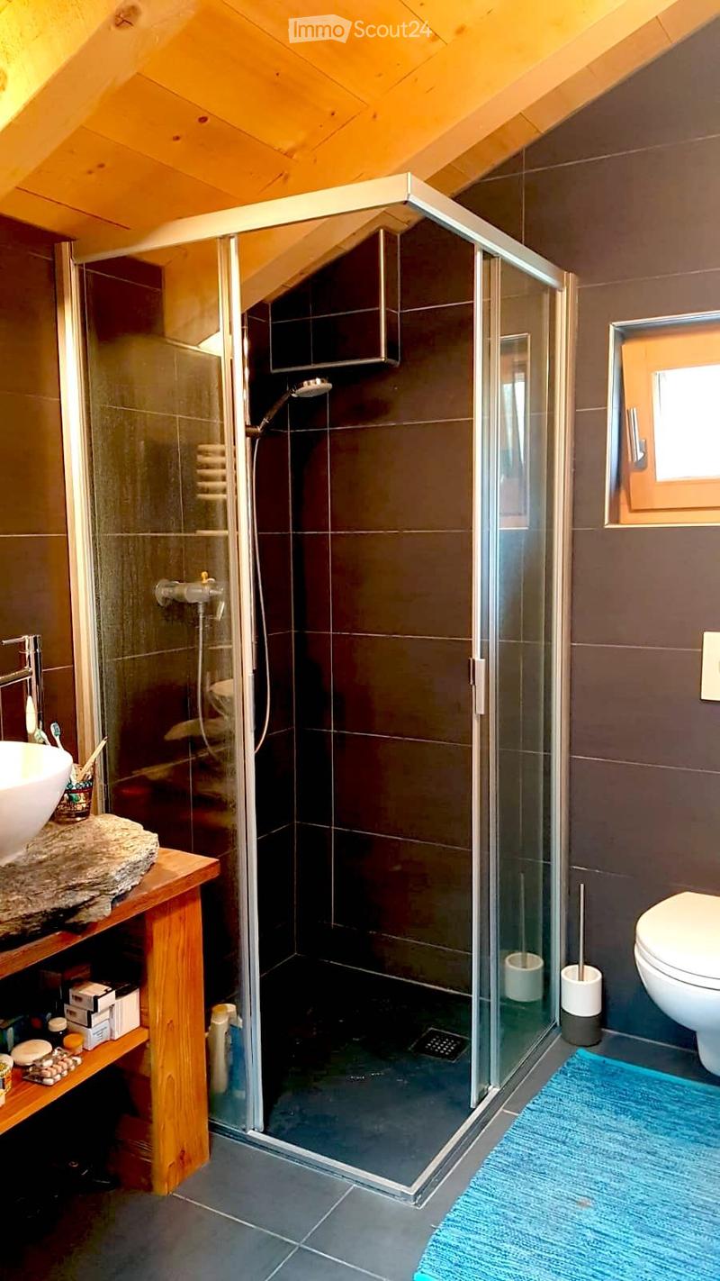 bathroom with a glass shower, white toilet, sink, blue rug, wooden shelf with toiletries, wooden table, wooden ceiling