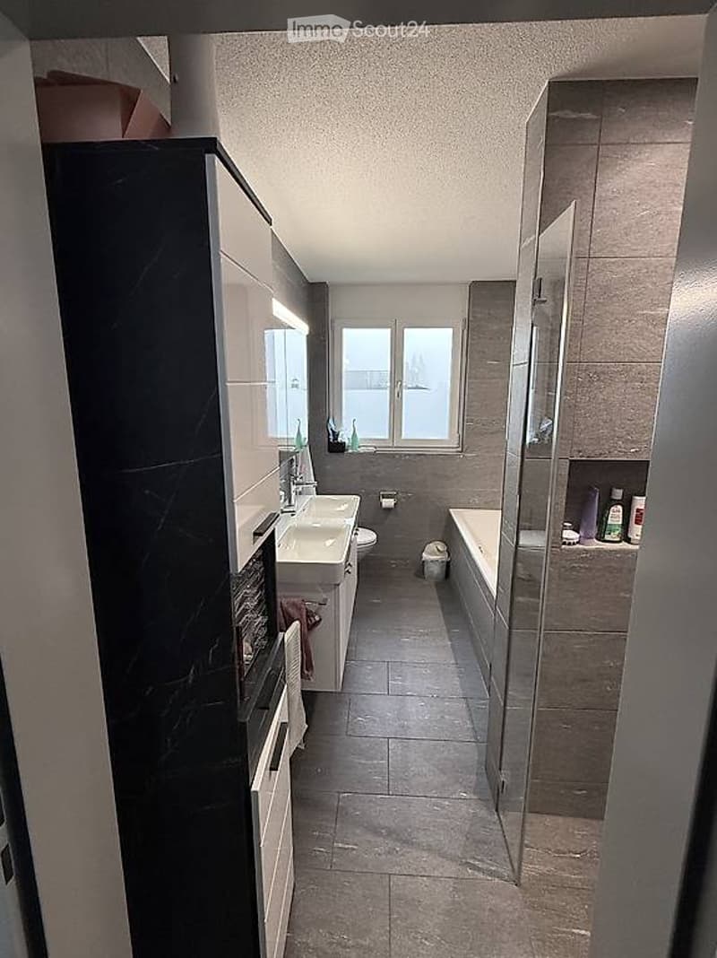 Modern bathroom with a large window, featuring a sink, toilet, bathtub, and a glass-enclosed shower. The space includes a mirrored cabinet and a towel hanging on the wall.