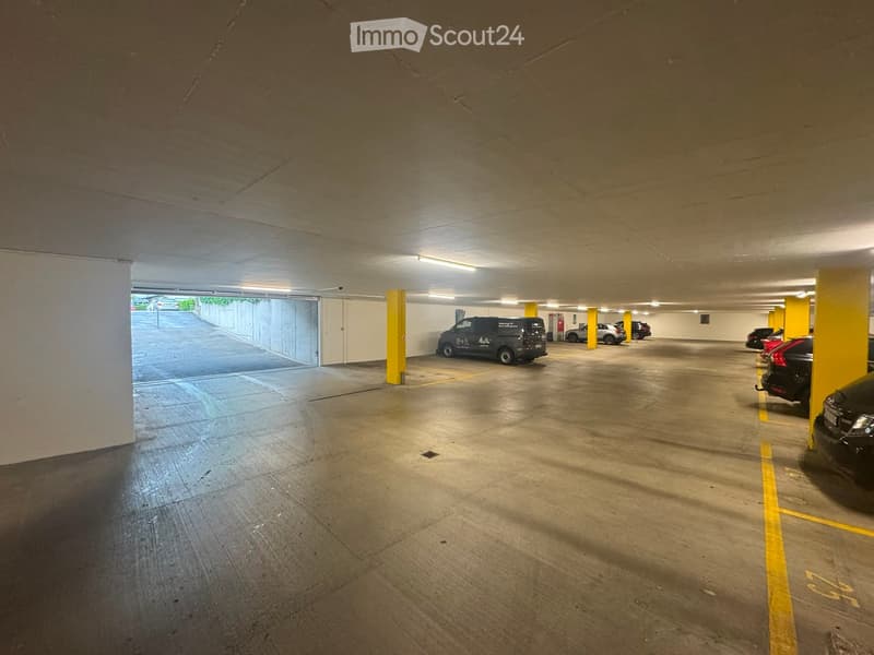 Underground parking area with several parked cars, yellow pillars, and concrete floors.