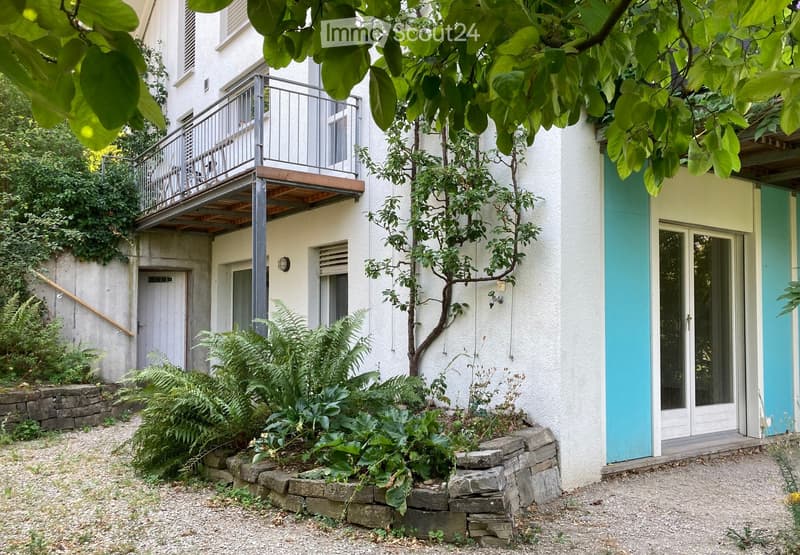 Garden area with lush greenery, stone walls, and a raised balcony overlooking the space.