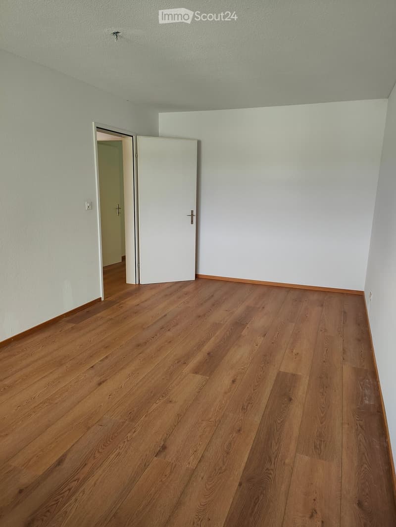 Empty room with light-colored walls and wooden flooring, featuring a partially open white door leading to another room.