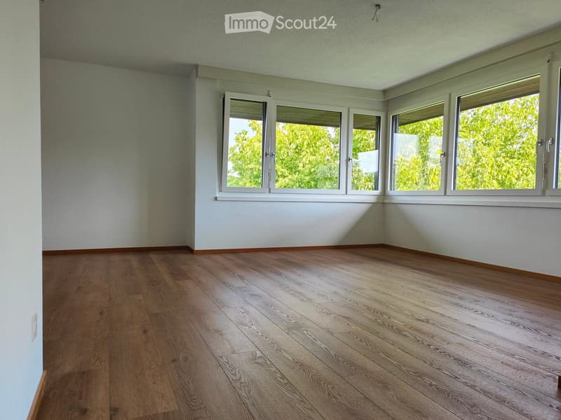 Empty room with wooden flooring and large windows, featuring light-colored walls and a clean, minimalist design.