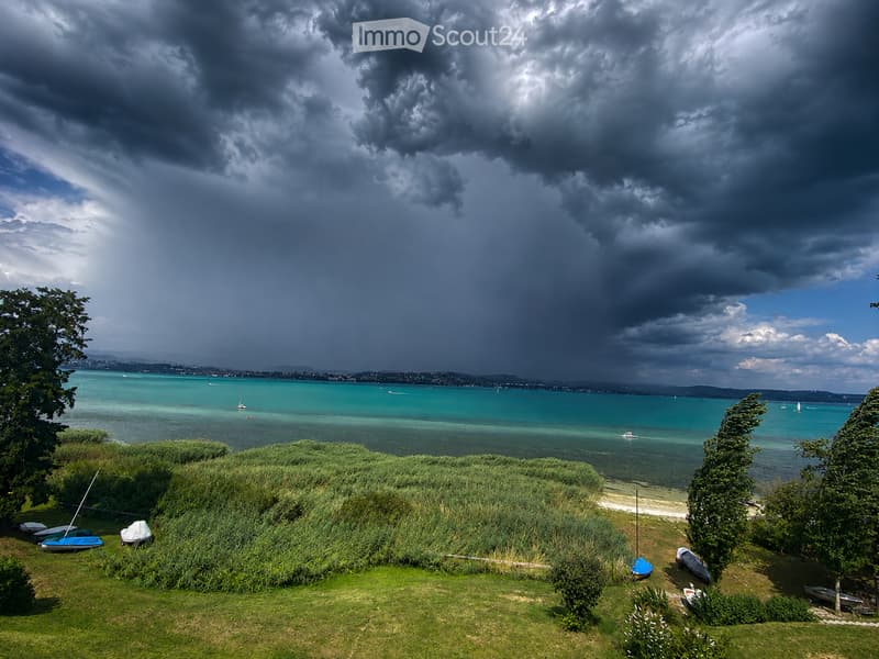 A scenic lakeside view with a grassy area, boats, and a dramatic sky.