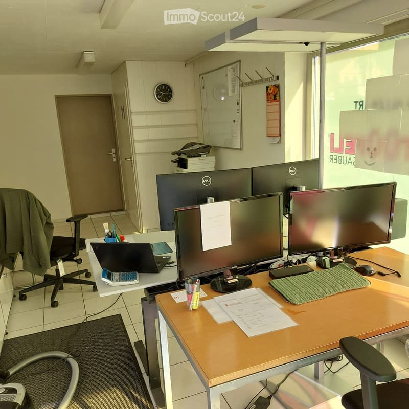 Office space with two desks, multiple computer screens, chairs, a laptop, a printer, and various office supplies.