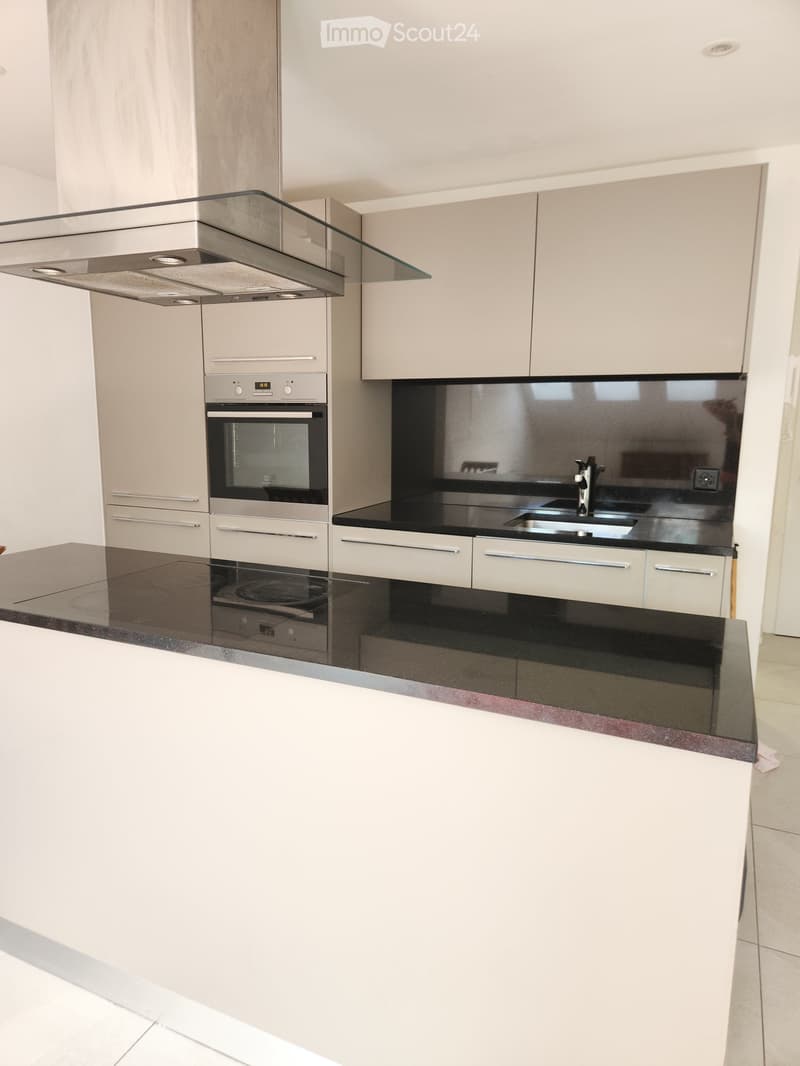 Modern kitchen with white cabinets, black countertops, stainless steel appliances, and a central island.