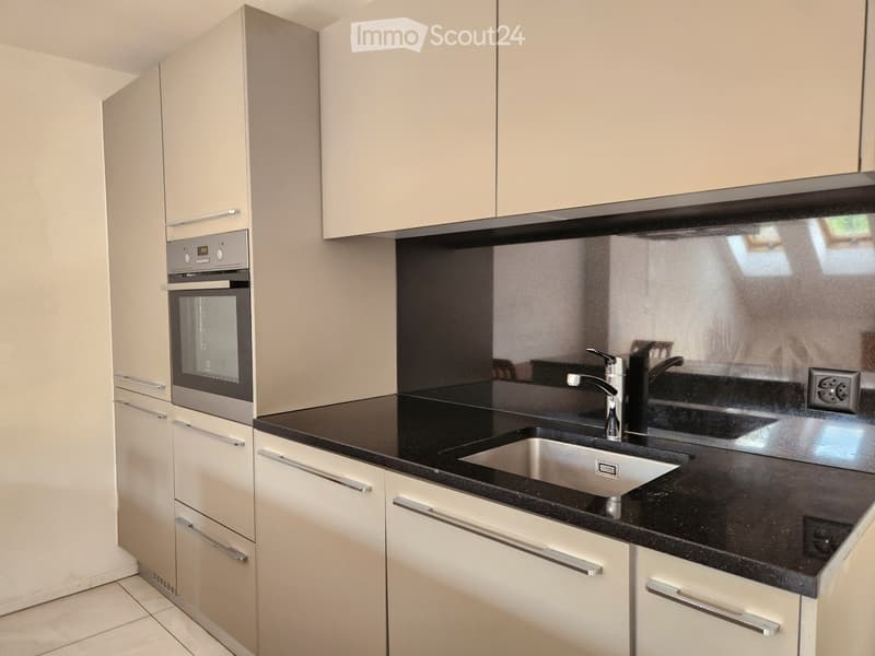 Modern kitchen with white cabinets, black countertop, stainless steel sink, and built-in oven.