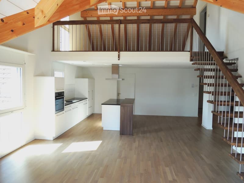 Open-plan kitchen with light wooden flooring, white cabinets, a central island, and a staircase leading to an upper level.