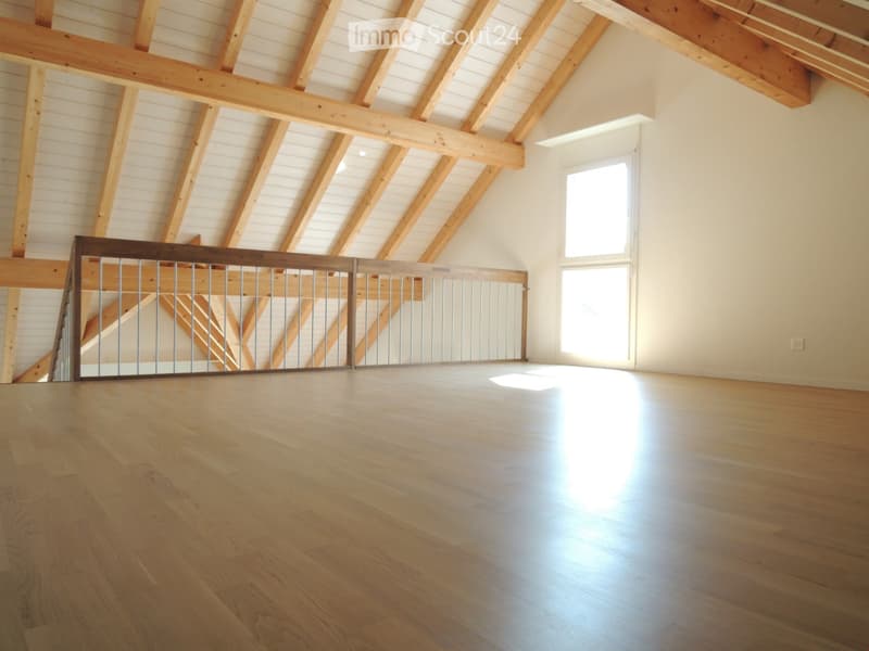 Empty room with exposed wooden beams, wooden flooring, and a metal railing leading to a staircase.