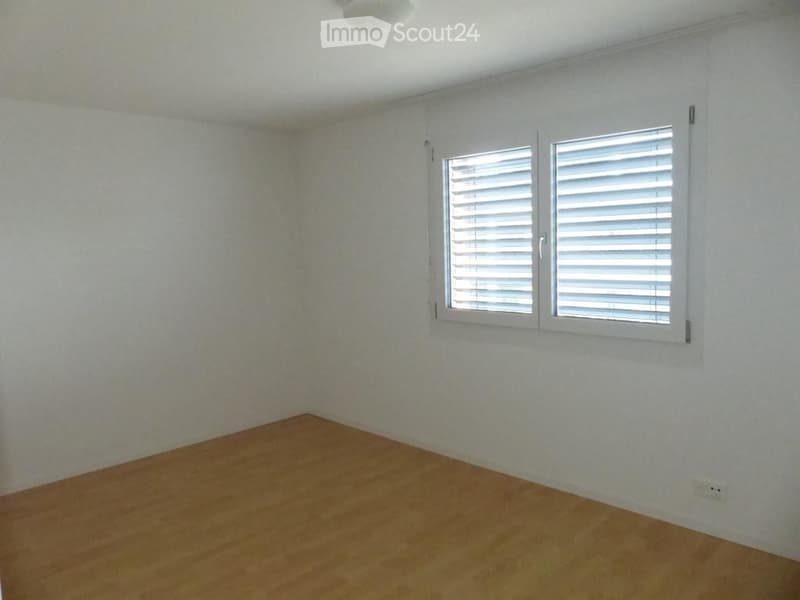 Empty room with wooden flooring, white walls, and a window with white shutters.