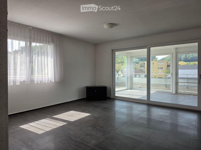 Empty room with tiled floor, large sliding glass doors leading to a balcony, and white walls with sheer curtains on the windows.