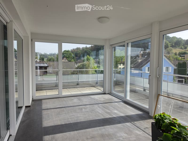 Spacious balcony with large glass sliding doors, tiled floor, and a view of the surrounding neighborhood and greenery.