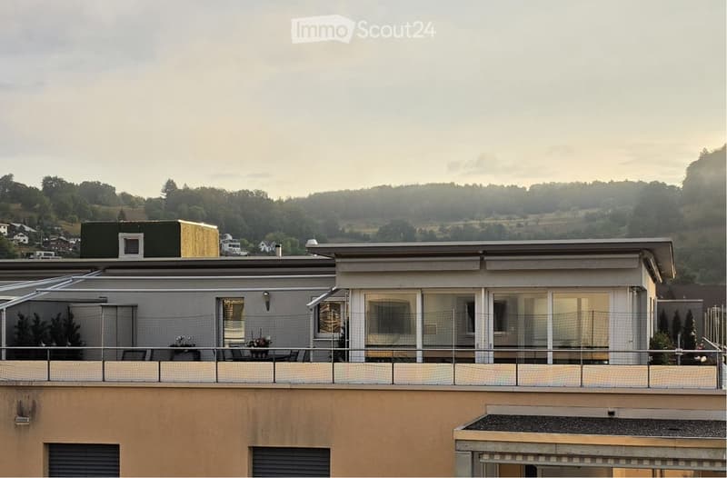 Balcony with a table and chairs, overlooking a scenic landscape with trees and hills.