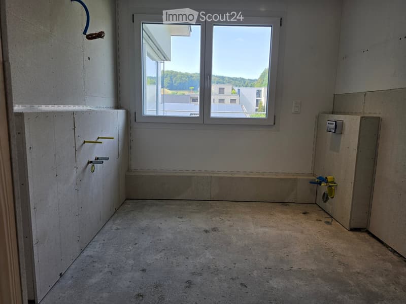 Empty room with concrete floor, white walls, and large windows offering a view of the surrounding area.