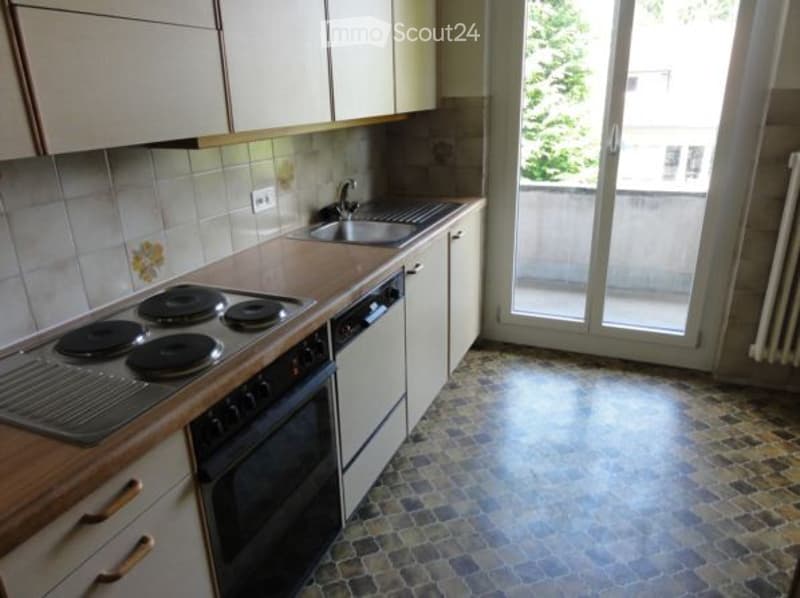 Kitchen with electric stove, oven, sink, and cabinets, leading to a balcony.