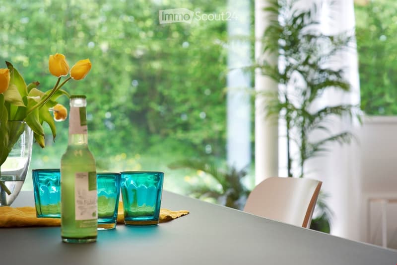 desk with flower vase, 3 glasses, bottle, chairs, windows with plant view