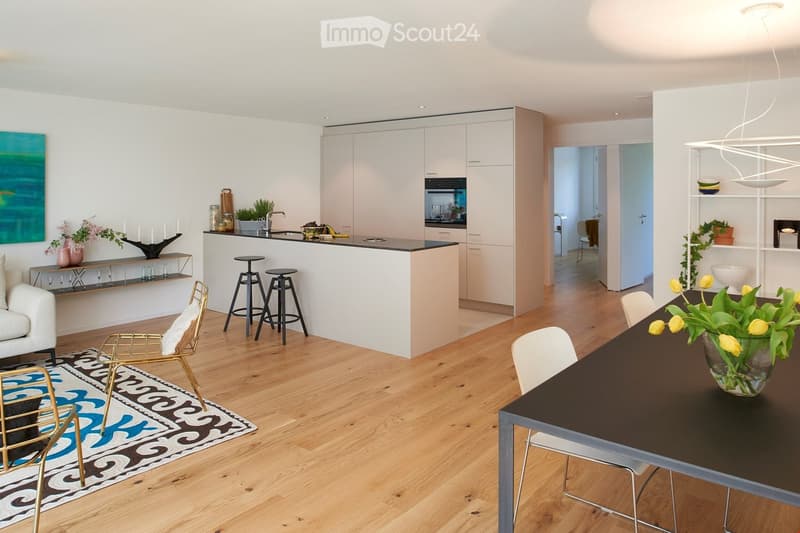 Modern kitchen with island counter, white cabinets, black countertops, open layout with dining area, hardwood floors, large windows, decorative items, and artwork.