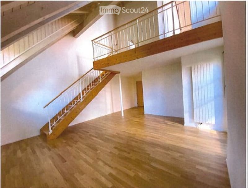 Empty room with wooden flooring, white walls, and a staircase leading to an upper level with a wooden railing.