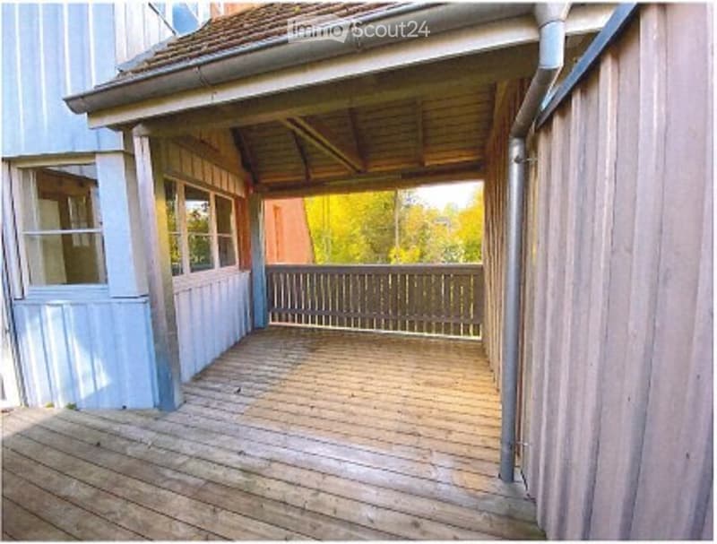 Wooden deck with a simple wooden railing, attached to a house with light blue siding and white trim.