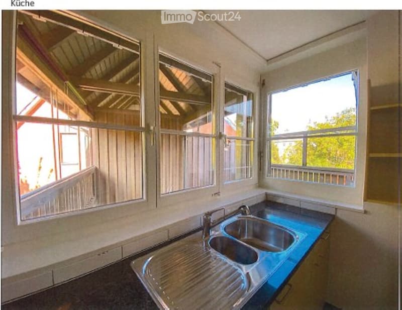 Empty kitchen with stainless steel sink, multiple windows, and blue countertop.