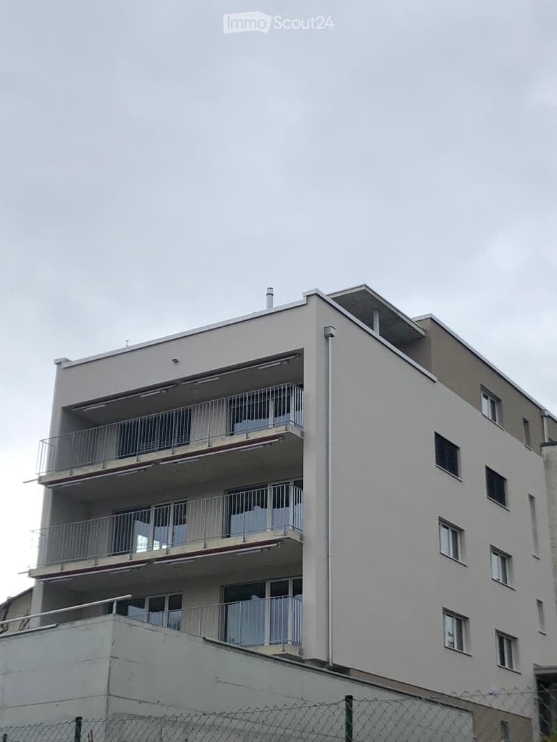 Four-story residential building with multiple balconies and windows, featuring a flat roof and a chimney.