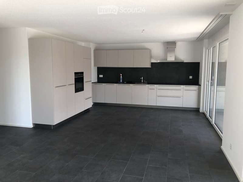Modern kitchen with white cabinets, black countertop, and dark tiled floor. Features an oven, sink, and faucet.