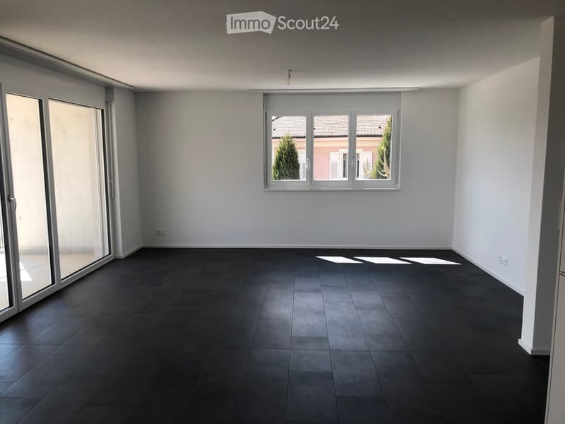 Empty room with dark tiled floor, white walls, large sliding glass door, and window with view of neighboring building.