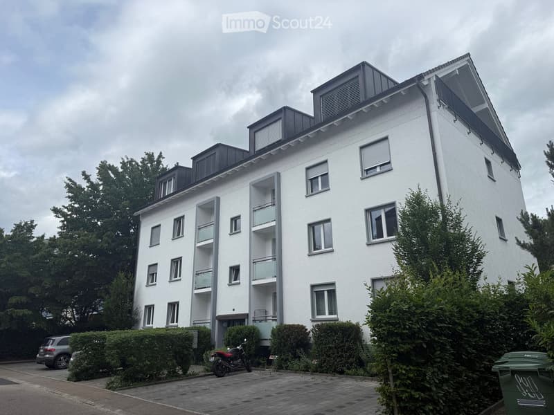 Modern multi-story residential building with white facade, multiple balconies, and contemporary design. Features include large windows, a flat roof with modern roofing, and surrounding greenery.