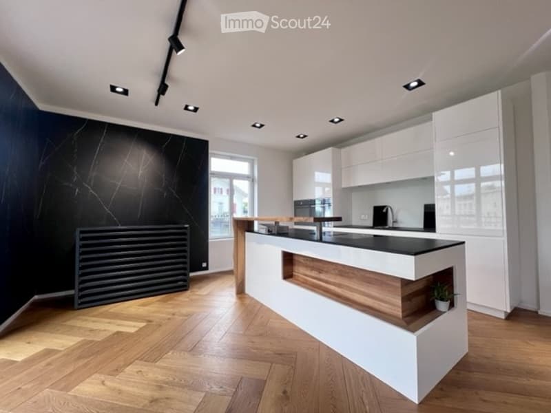 Modern kitchen with white cabinets, black countertops, wooden flooring, and built-in appliances.