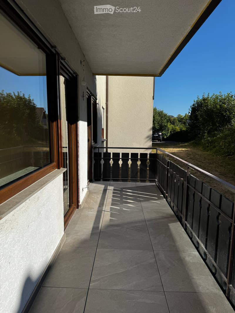 Balcony with tiled floor, black metal railing, and large window with wooden frame on one side.
