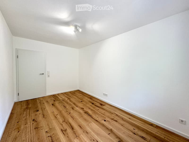 Empty room with light wooden flooring, white walls, and a single door. No furniture or equipment is present.
