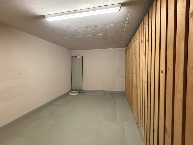 Empty hallway with wooden paneling on one side, concrete floor, and a single door at the end.