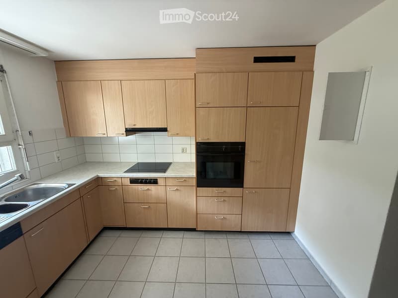 Modern kitchen with light wooden cabinets, stainless steel sink, and built-in oven.