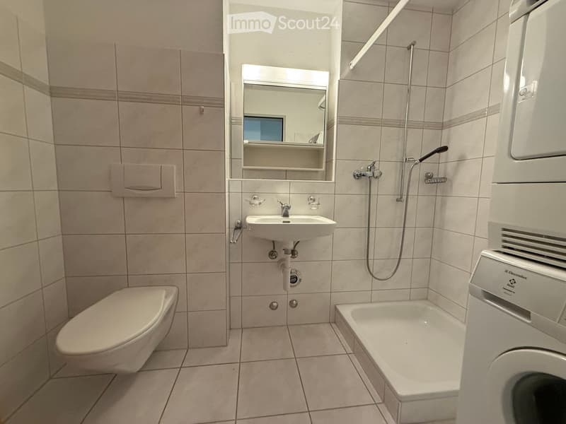 Modern bathroom with beige tiles, a toilet, a sink, a bathtub, a mirror, and a showerhead.