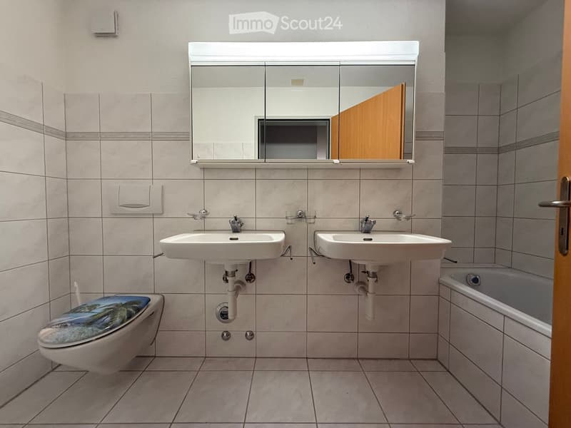 Modern bathroom with two sinks, a toilet, a bathtub, and a large mirror above the sinks.