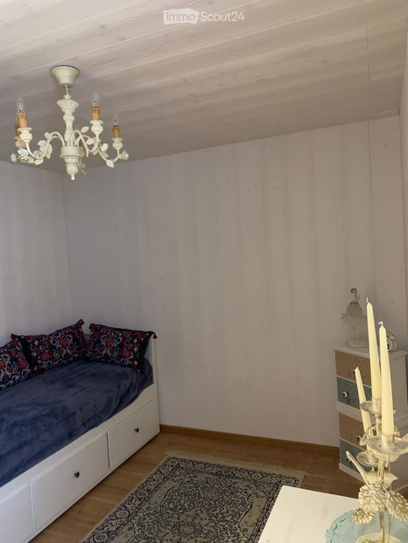 Cozy room with a daybed, patterned pillows, a chandelier, a small table with candles, and a patterned rug.