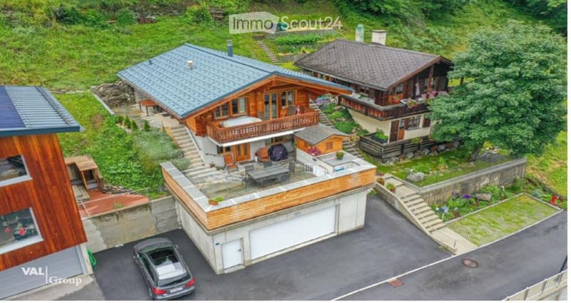 Aerial view of a multi-level house with a garage, parking area, and swimming pool, surrounded by greenery and neighboring houses.