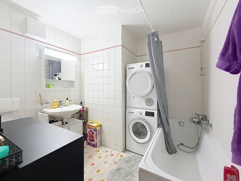 Bathroom with white tiled walls, a sink with mirror, a bathtub, and a stacked washing machine/dryer unit.