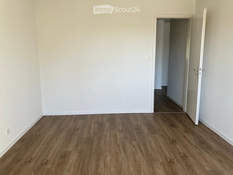 Empty room with light-colored walls and wooden flooring, featuring an open doorway leading to another room.