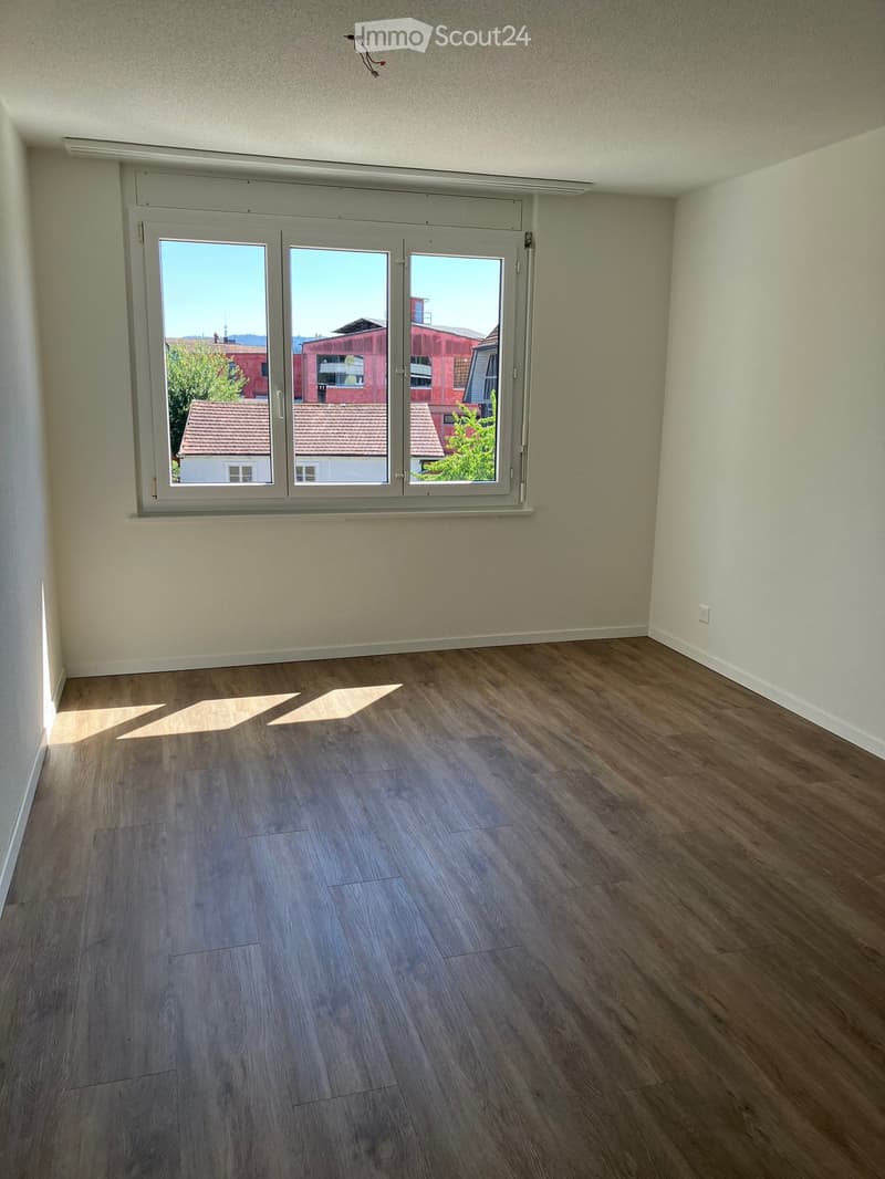 Empty room with wooden flooring and large window offering a view of the outside. No furniture or equipment present.