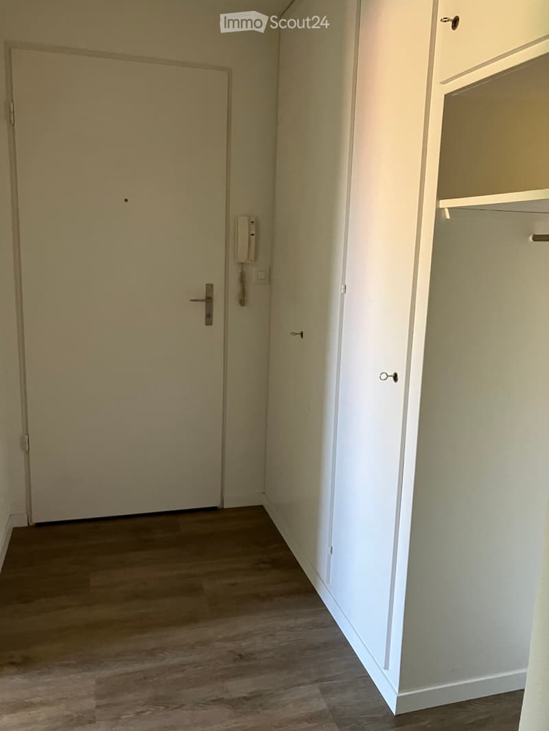 Empty hallway with wooden flooring, white walls, and a closed door on the left. A small cabinet is visible on the right side.