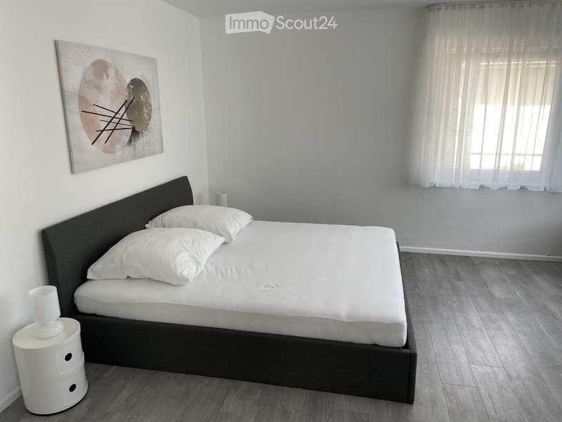 Modern bedroom with a double bed, white bedding, a nightstand with a lamp, and a contemporary painting on the wall.
