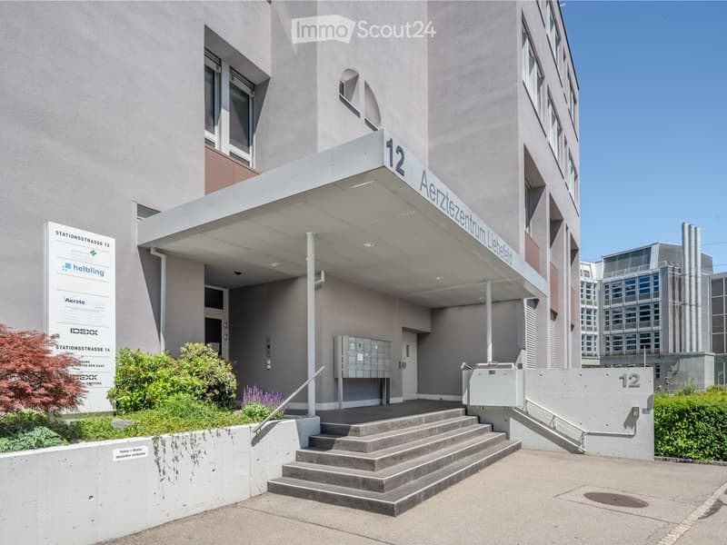 Modern building entrance with a covered walkway, steps, and signage reading "Aerztezentrum Liebfeld."