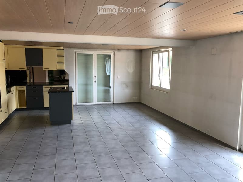 Modern kitchen with light-colored cabinets, a central island, and tiled flooring. Features a large window and a sliding glass door leading to an outdoor area.
