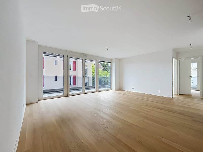 Empty room with light wooden flooring, white walls, and large sliding glass doors leading to a balcony.