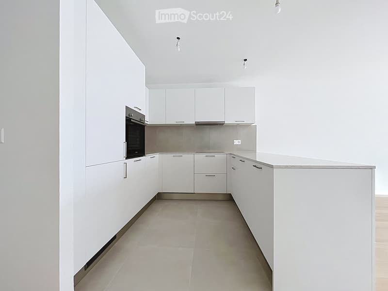 Modern, minimalist kitchen with white cabinets, stainless steel appliances, and a central island. The space is empty, with no furniture or appliances installed.