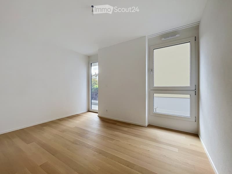 Empty room with light wooden flooring, white walls, and large windows with blinds. No furniture or equipment is present.