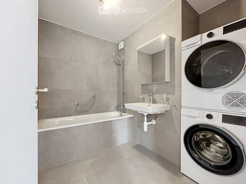 Modern bathroom with a bathtub, sink, mirror, and a stacked washer/dryer unit.