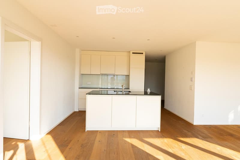 Modern kitchen with white cabinets, a central island, and wooden flooring. The space is bright with natural light and features a sleek, minimalist design.