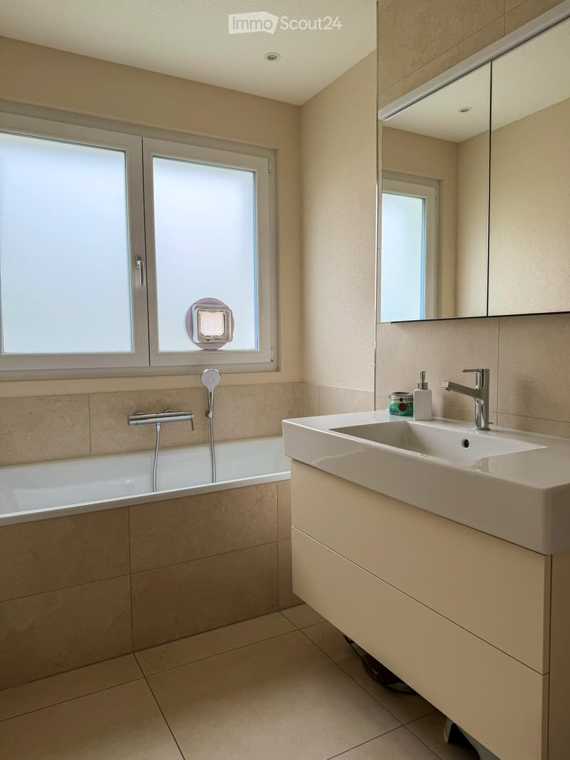 Bathroom with bathtub, shower head, sink, soap dispenser, mirror, and window.